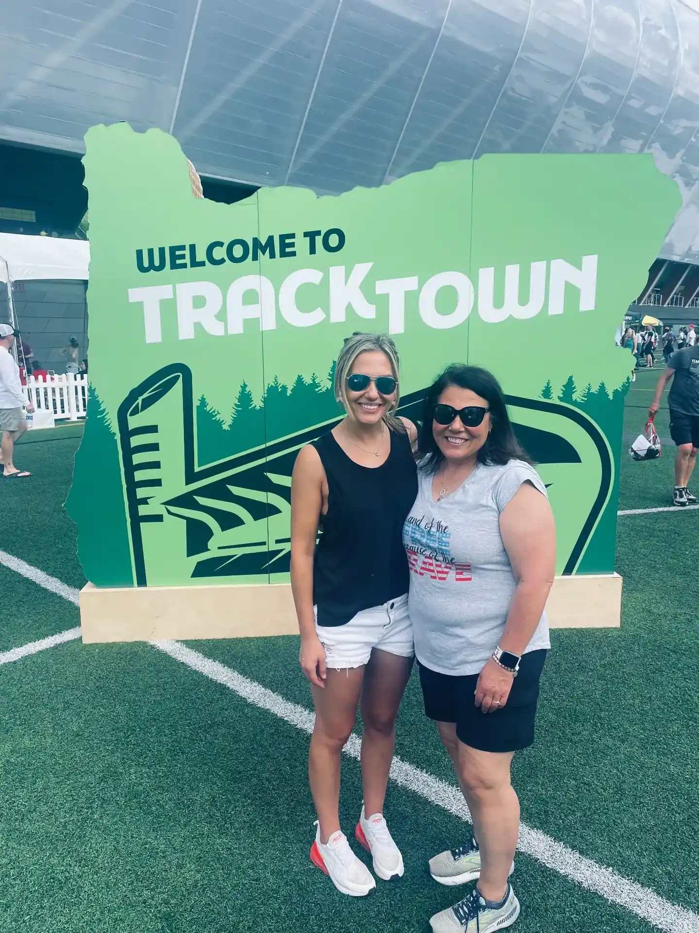 Two women smiling beside a Welcome to TrackTown sign